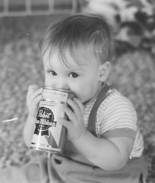 Front view of an infant sitting on the floor and holding a Pabst Blue Ribbon can to their mouth - black & white image